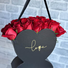 Red roses in a black heart-shaped box with a "love" label