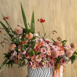 Large peach and pink floral arrangement in a white ribbed vase