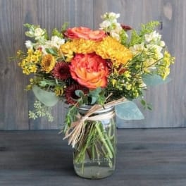 Mixed bouquet of orange, yellow, and white flowers in a glass jar