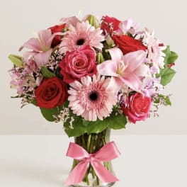 Bouquet of pink and red flowers in a clear glass vase with a pink ribbon