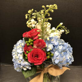 Bouquet of red roses and blue hydrangeas in a glass vase with a burlap bow