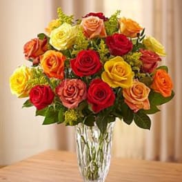 Mixed roses in red, yellow, orange, and pink arranged in a clear glass vase