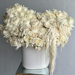 White rose arrangement in a textured white vase with trailing white accents