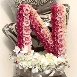 Pink rose arrangement shaped like the letter N with white orchids at the base.