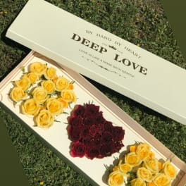 Long box of yellow and burgundy roses on grass