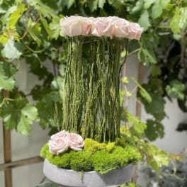 Pink roses arranged in a tall moss-filled bowl with hanging greenery