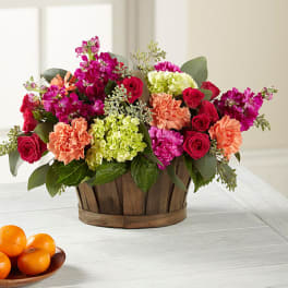 Mixed bouquet in a wooden basket with pink, red, peach, and green blooms