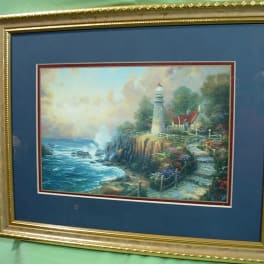 Framed lighthouse landscape painting on a blue mat
