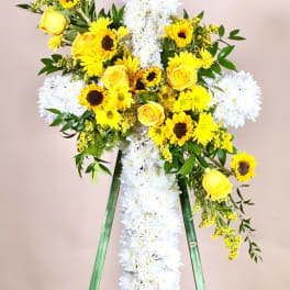 Yellow roses and sunflowers arranged on a white floral cross easel.