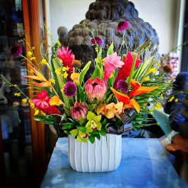 Tropical flower arrangement in a white vase with pink, orange, and yellow blooms