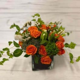 Orange roses arranged in a black square vase with greenery