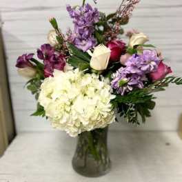 Mixed bouquet of white hydrangea, purple flowers, and roses in a glass vase