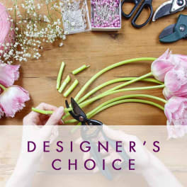 Pink tulips being trimmed on a wooden table with scissors and floral supplies