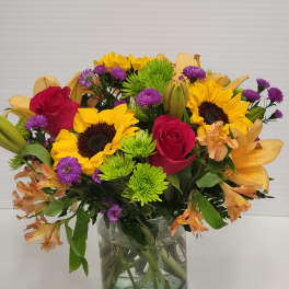 Mixed bouquet of sunflowers, red roses, and purple flowers in a glass vase