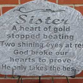 Gray memorial plaque with engraved tribute text against a brick wall