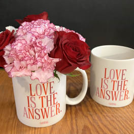 Red roses and pink carnations in a white mug beside a matching mug
