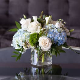 White roses and blue hydrangeas arranged in a clear glass vase
