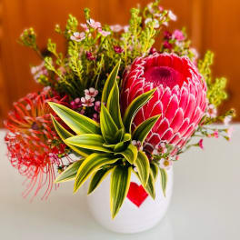 Bright tropical bouquet with a large pink protea in a white vase