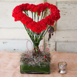 Red carnations arranged in a heart shape in a glass vase