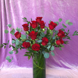 Red roses in a tall glass vase with eucalyptus foliage