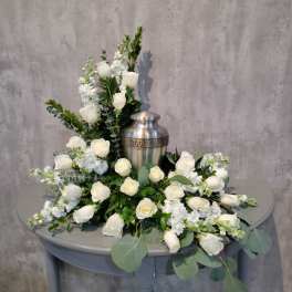 White roses and white flowers arranged around a silver urn on a table