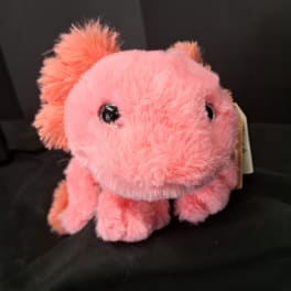 Pink plush dinosaur toy with black eyes on a dark background