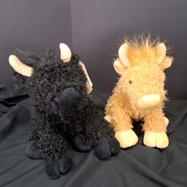 Two plush moose toys, one black and one tan, sitting on black fabric