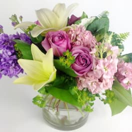 Bouquet of pink roses, lilies, and purple flowers in a glass vase