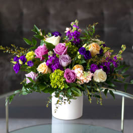 Mixed bouquet of roses and purple blooms in a white vase