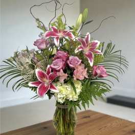 Pink lilies and roses in a glass vase with greenery