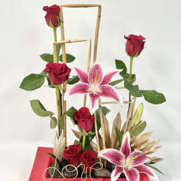 Red roses and pink lilies in a red rectangular vase with bamboo accents