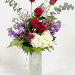 Red roses and purple flowers in a white vase
