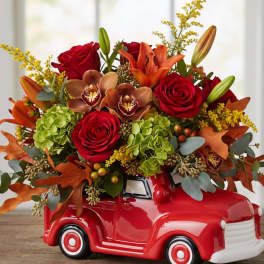 Autumn bouquet of red roses, orange lilies, and green hydrangeas in a red ceramic truck container