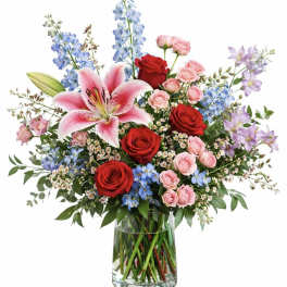 Bouquet of red and pink roses with lilies and blue flowers in a glass vase