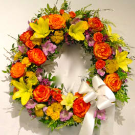 Circular floral wreath with orange roses, yellow lilies, and a white ribbon bow