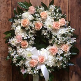 Round floral wreath with peach roses and white flowers on a wooden background