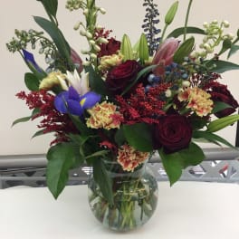 Mixed bouquet of roses, lilies, and irises in a glass vase