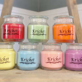 Seven colorful jar candles arranged on a wooden shelf