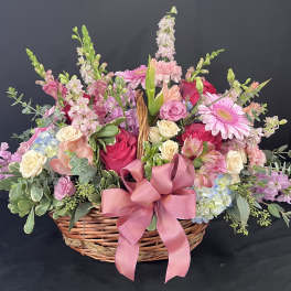 Basket arrangement of pink and cream flowers with a large pink ribbon