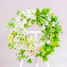 White floral wreath with green foliage on a stand
