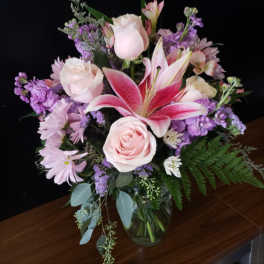 Pink roses and lilies arranged in a glass vase with purple flowers