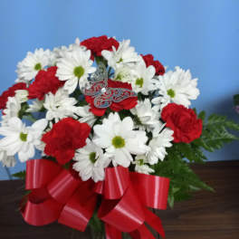 Red carnations and white daisies in a vase with a red bow and silver butterfly accent.