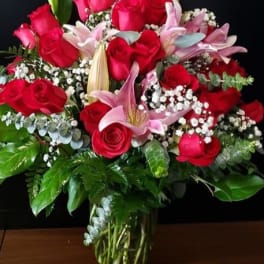 Tall glass vase of red roses, pink lilies, and white filler flowers in a full rounded bouquet
