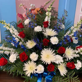 Large red, white, and blue floral arrangement in a basket with a blue ribbon