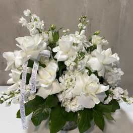 White floral arrangement in a glass vase with ribbon streamers