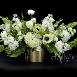 White floral arrangement in a gold vase with green accents