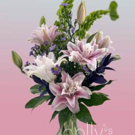 Pink and white lilies in a clear glass vase with purple accents