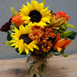 Bouquet of sunflowers, orange lilies, and mums in a glass vase
