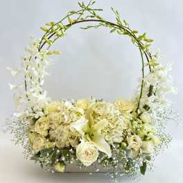 White floral basket arrangement with roses and orchids on an arched handle