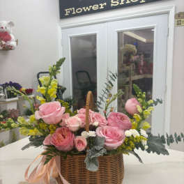 Pink roses and yellow snapdragons in a wicker basket with ribbon